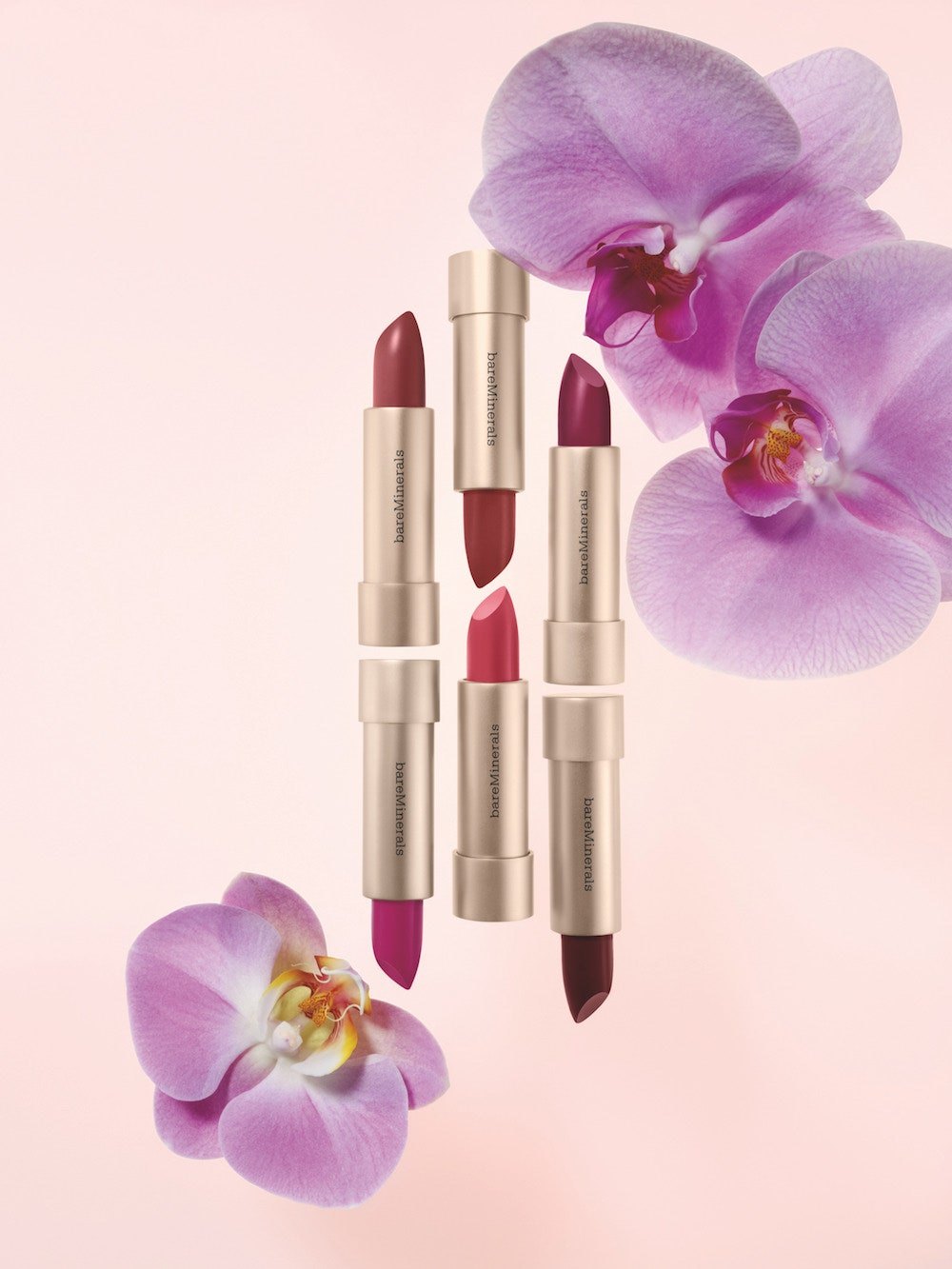 Four Mineralist lipsticks among lilac orchids on pink