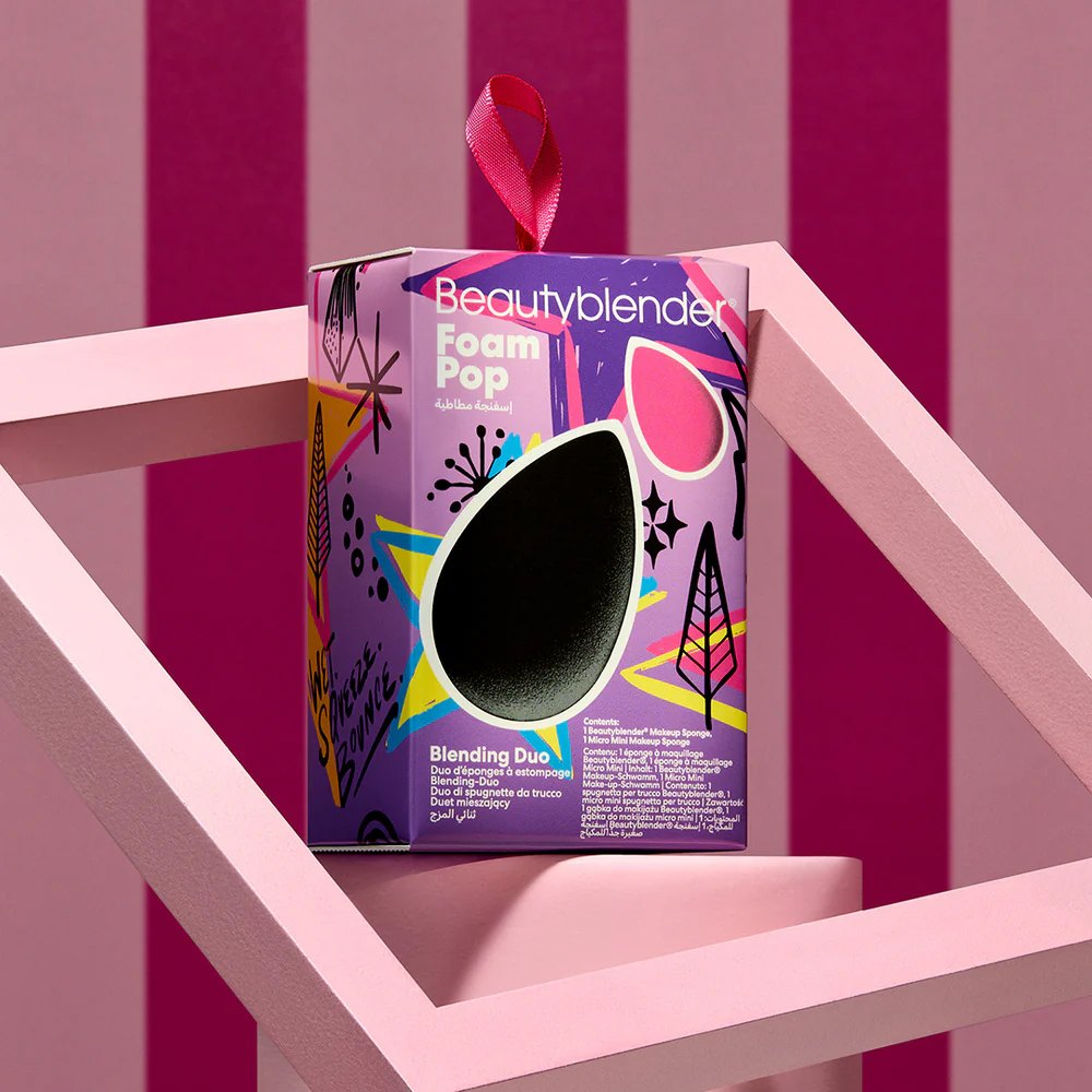 The Foam Pop box hanging by its ribbon inside a pink frame, against magenta stripes
