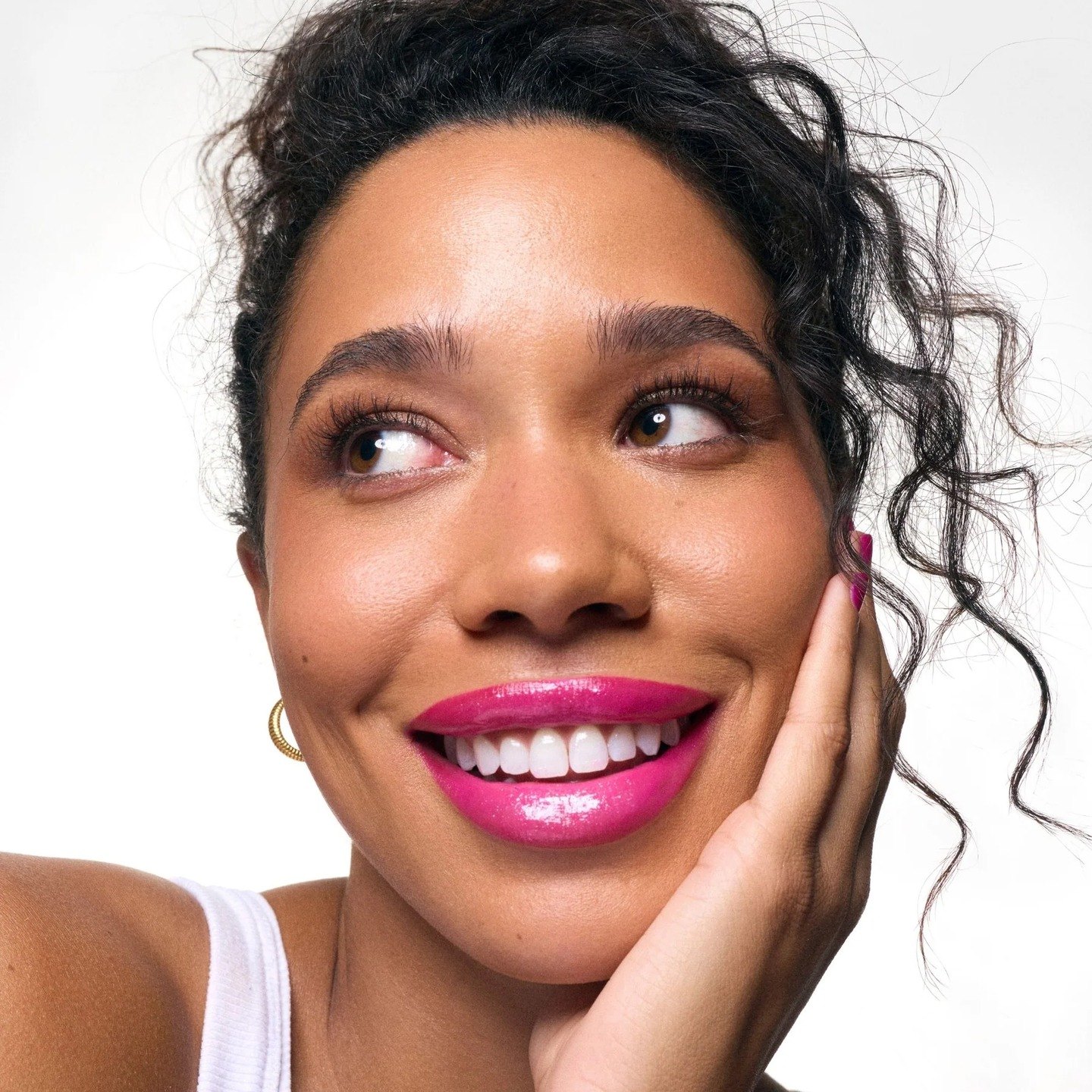 A woman smiling, hand to her cheek, pink gloss lip
