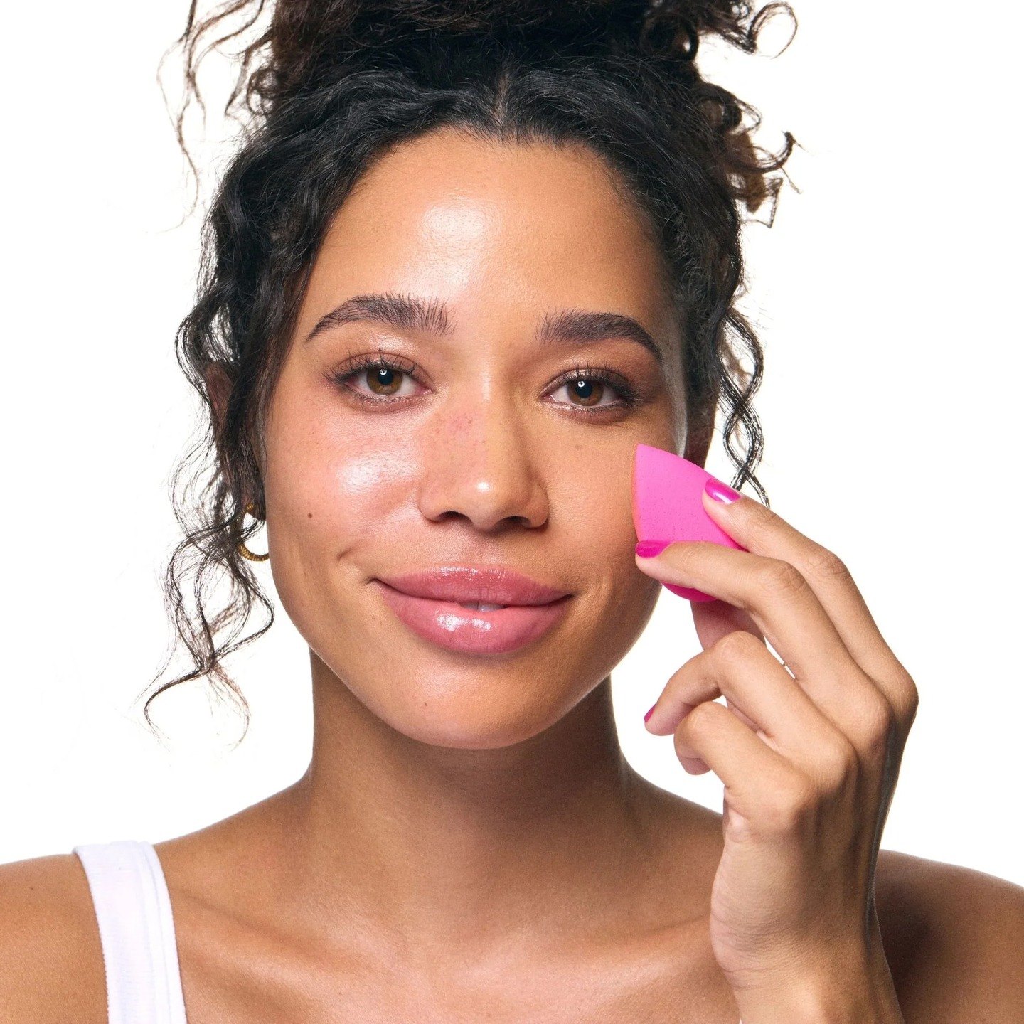 A woman pressing a pink Beautyblender sponge to her cheek