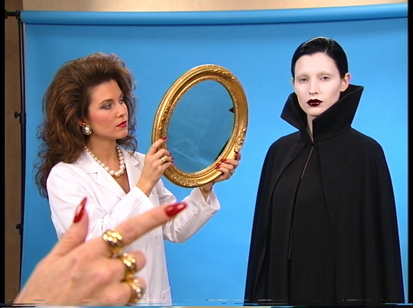 Storyboard, Ageless: a lab coat holds up a gold mirror to a pale vampire in a high collared black cape on a blue set