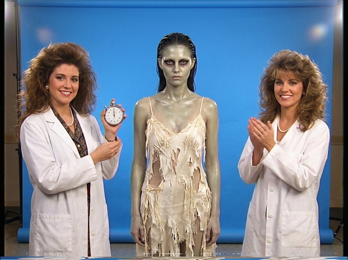 Storyboard, Drop-Dead Gorgeous: a zombie model in a shredded gold dress stands between two lab coats, one holding a stopwatch