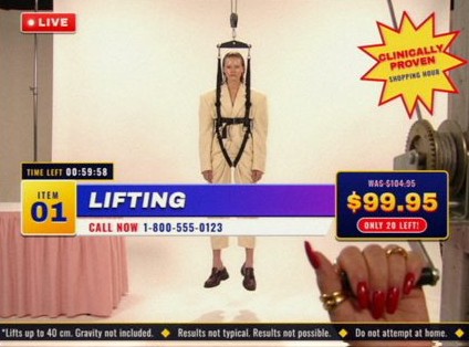 Style frame, item 01, Lifting: a model in a cream suit hangs in a harness from a winch while a hand with red nails turns the crank