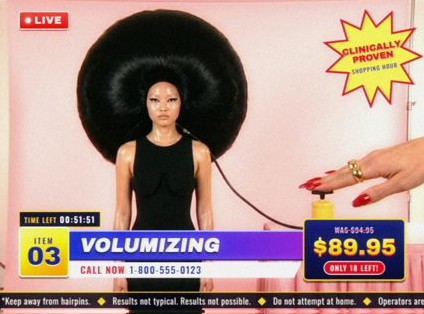 Style frame, item 03, Volumizing: a model with an enormous round black hairdo while a hand presses a yellow foot pump