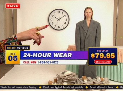Style frame, item 05, 24-Hour Wear: a model in a long grey coat beside a wall clock, newspapers and coffee cups piled at her feet