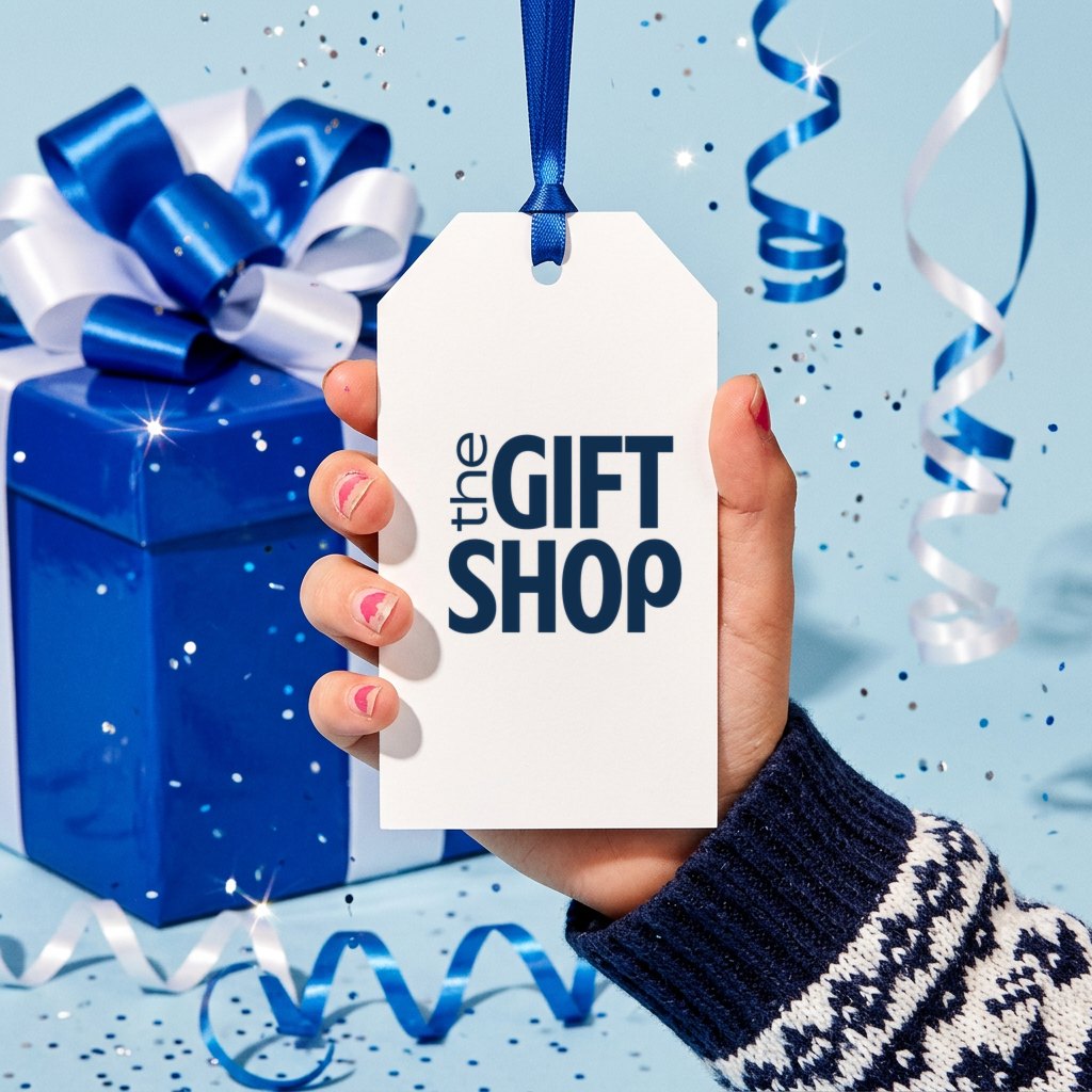 A hand in a Fair Isle sleeve holding a gift tag printed with The Gift Shop mark