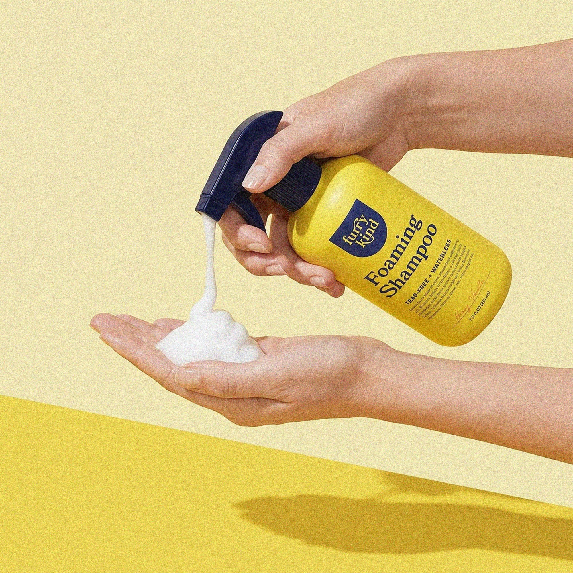 Foaming Shampoo pumped into a hand against yellow