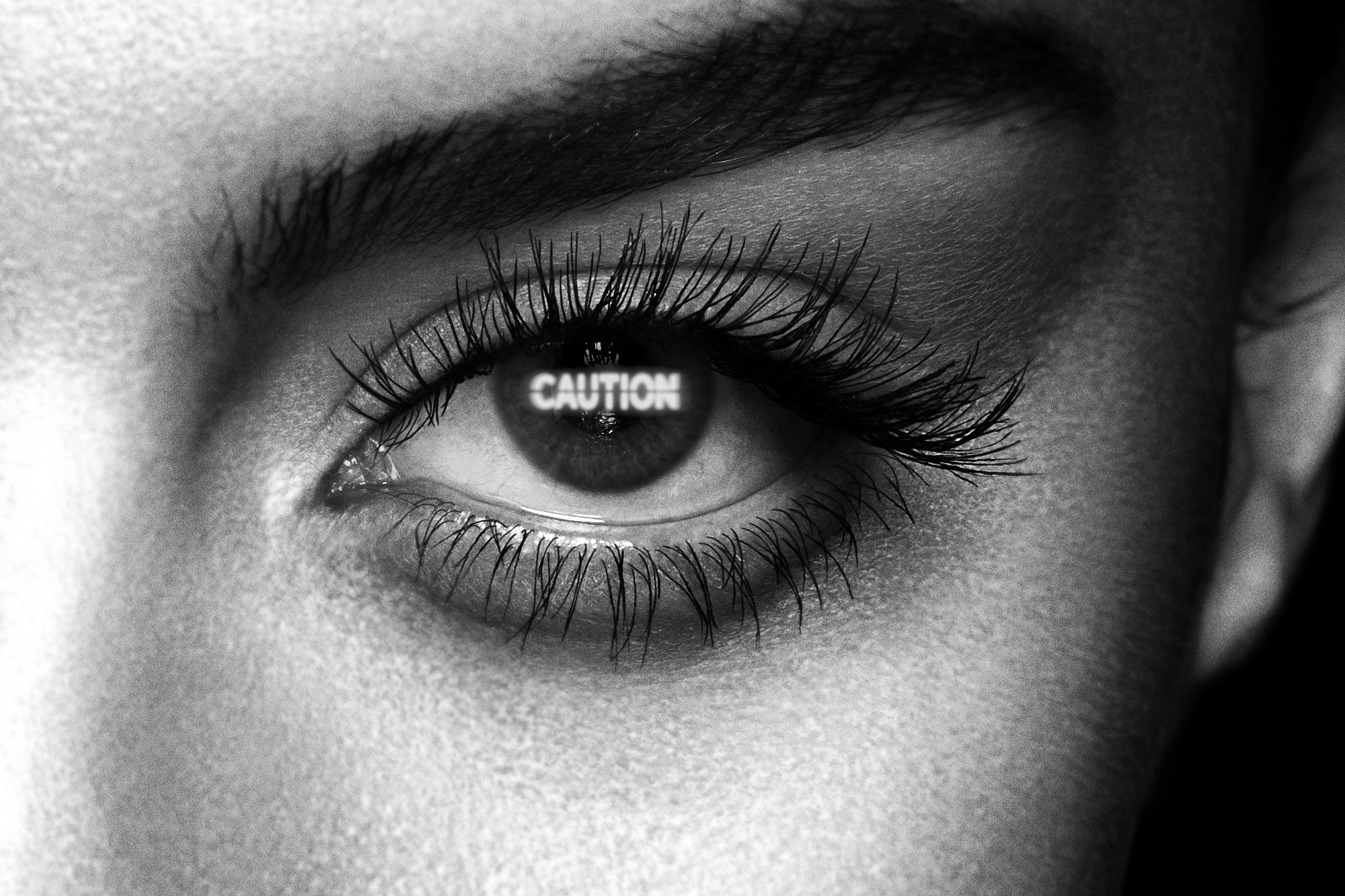 Close-up of an eye with heavy lashes, CAUTION reversed out across the pupil