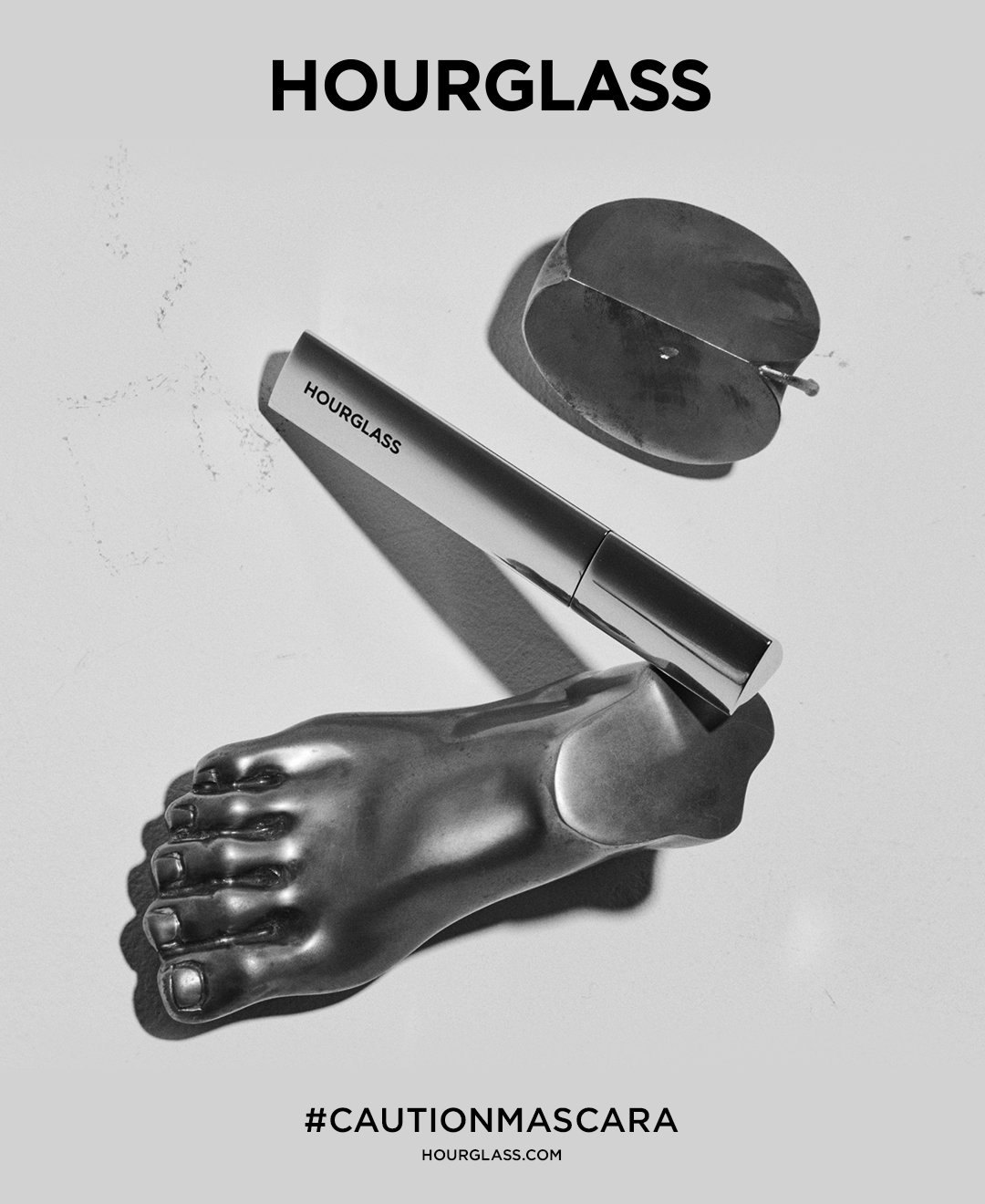 Poster: a silver sculpted foot, a compact and the mascara on pale gray, HOURGLASS above