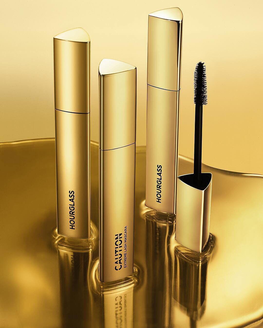 Instagram post: three gold CAUTION mascaras and a wand rising from liquid gold
