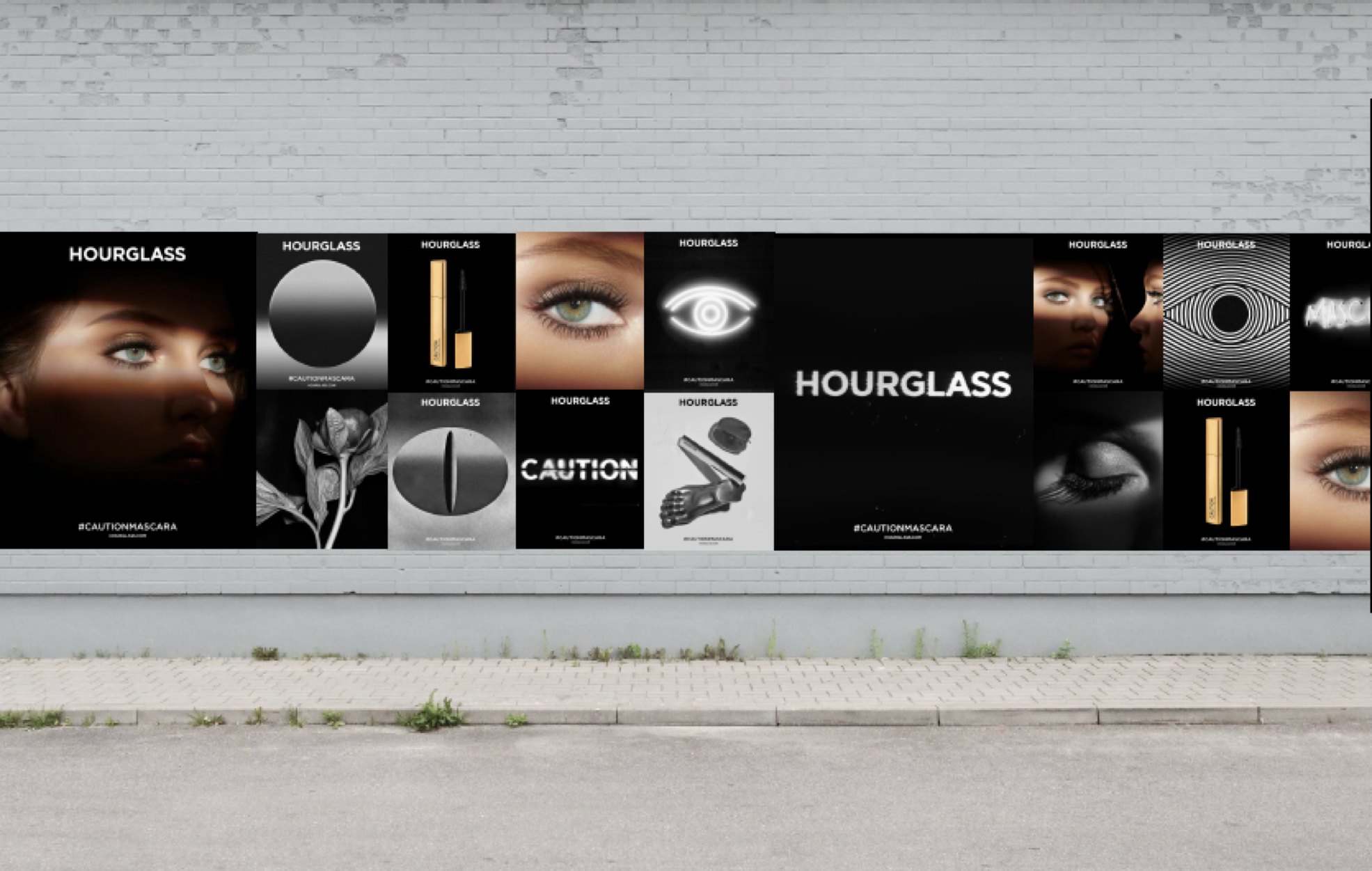 Mockup: the CAUTION poster grid along a pale brick wall: eyes in light, the gold mascara, the eye symbol, art stills, CAUTION and HOURGLASS