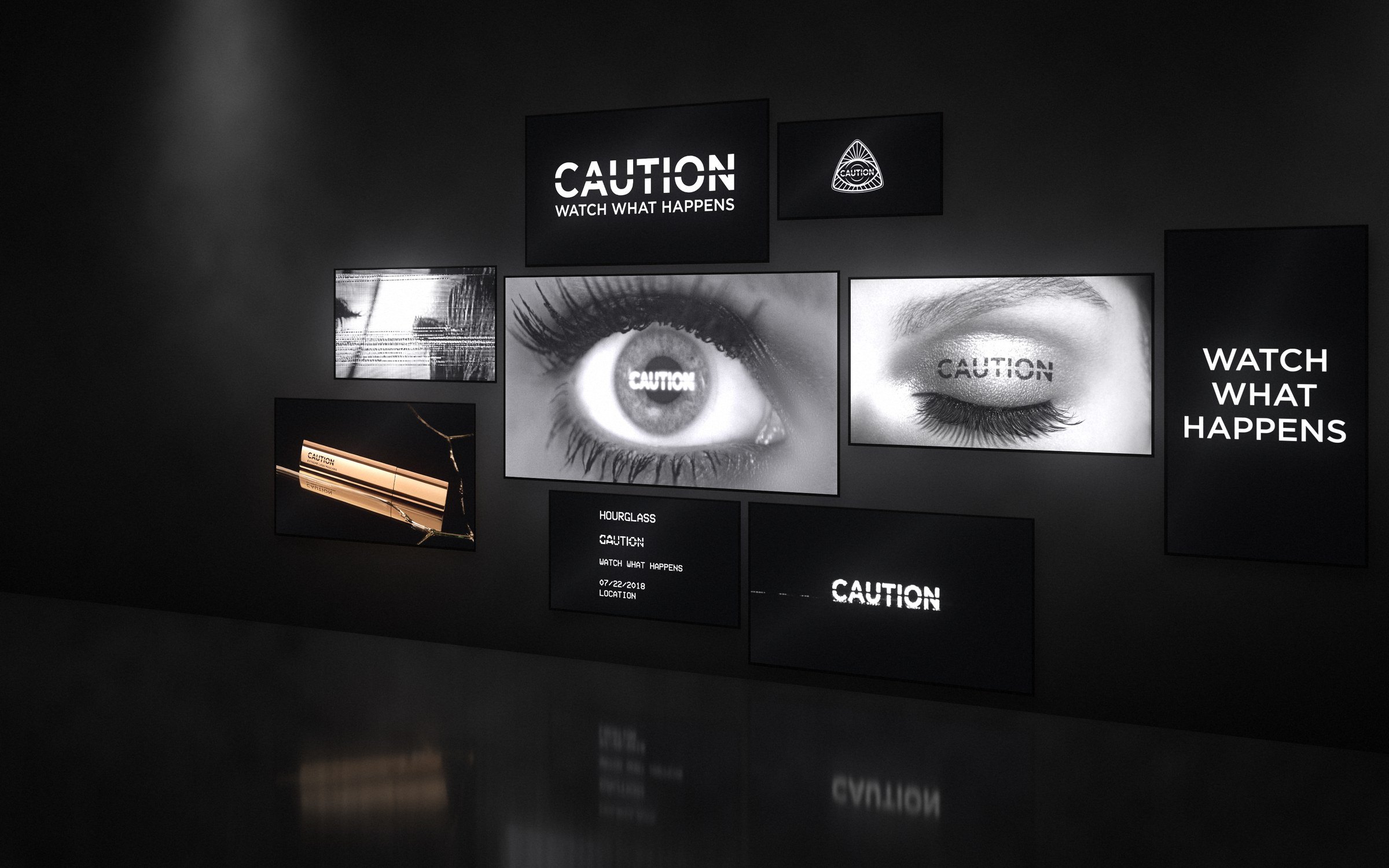Mockup: a cluster of screens on a dark wall showing the CAUTION eye, CAUTION on a closed lid, the mascara on broken glass, the seal, the invitation and WATCH WHAT HAPPENS, reflected in a glossy floor