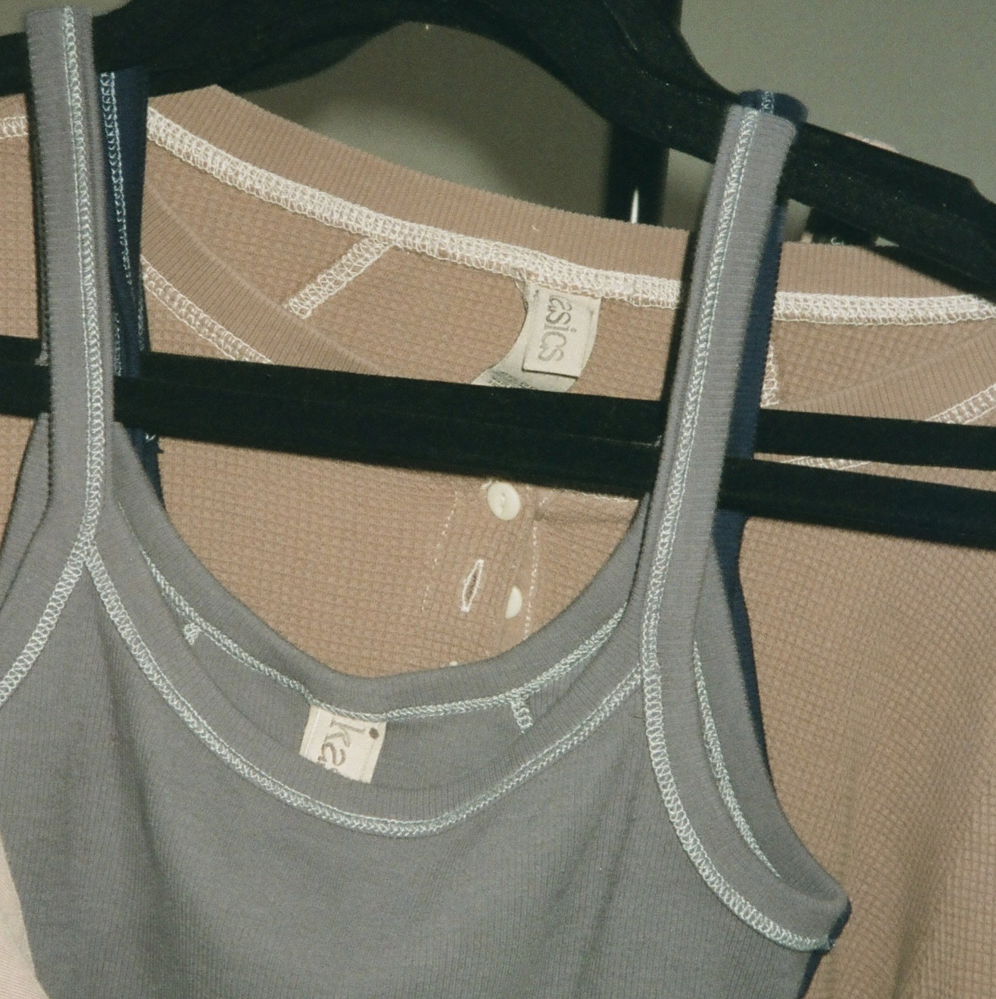 A grey tank over a waffle top on black hangers, each with a kasics neck label