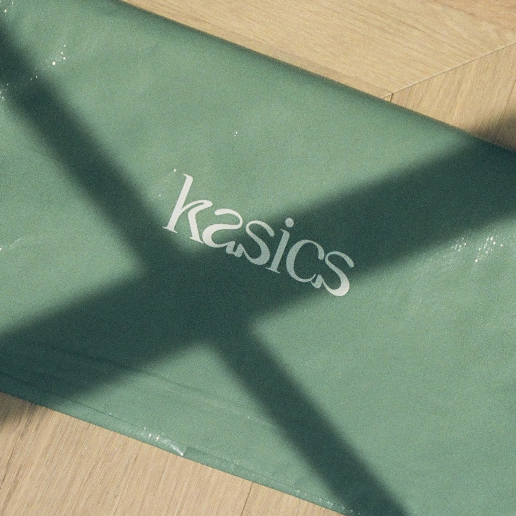 Sage tissue paper printed with the kasics wordmark, crossed by a window shadow