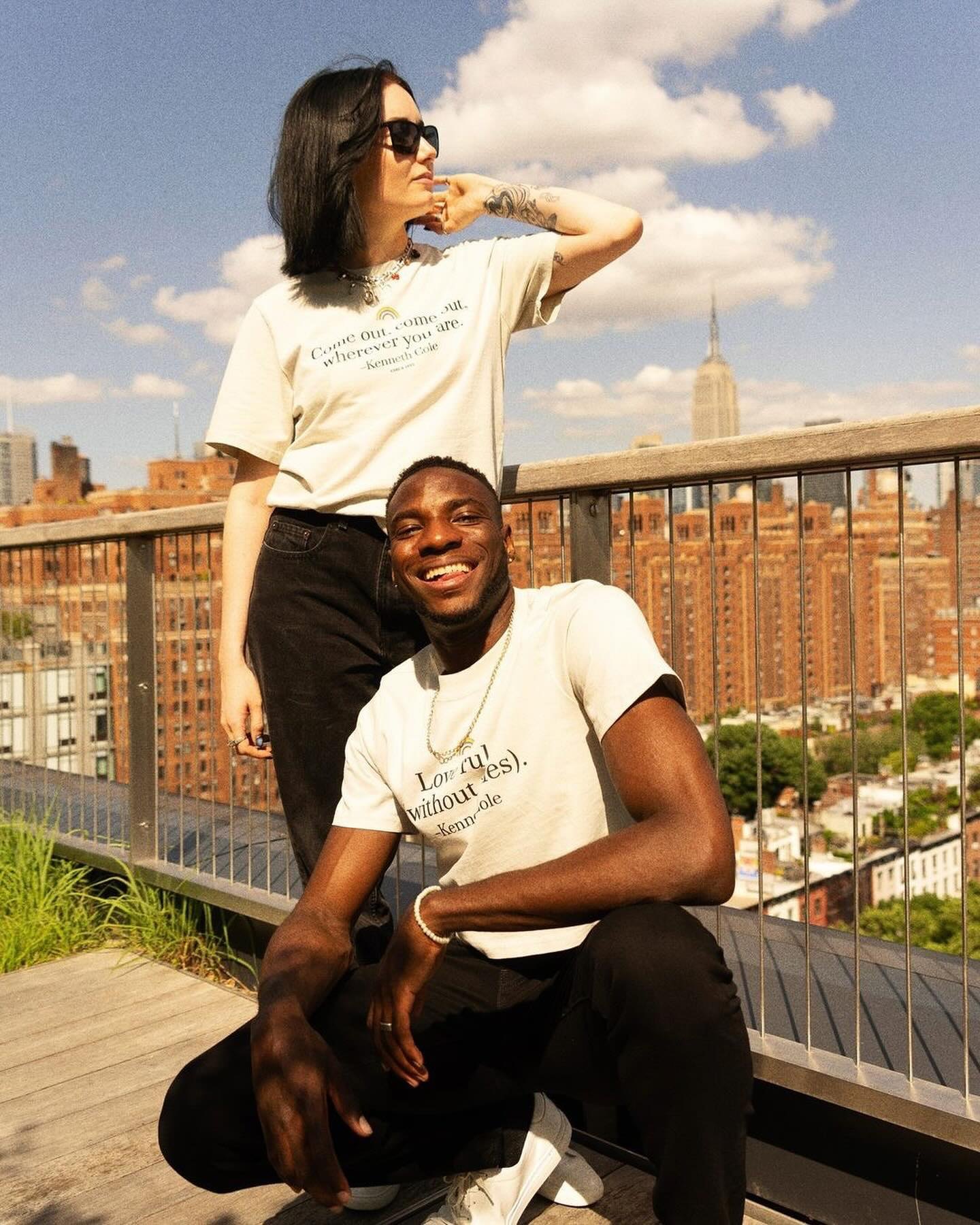 Two friends in the Pride tees on a rooftop over the city