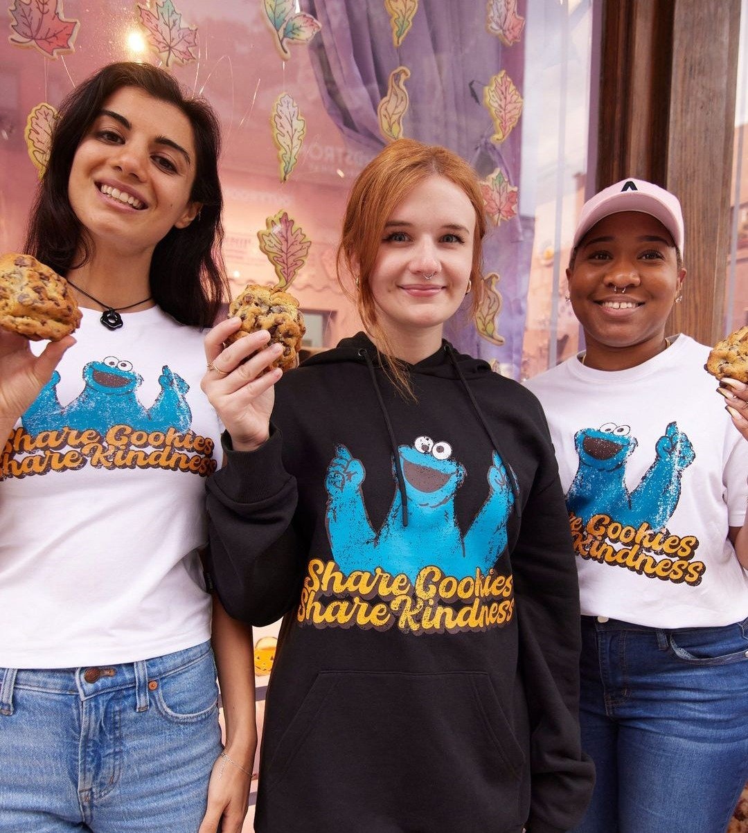 Three bakers holding cookies in Cookie Monster tees and a hoodie