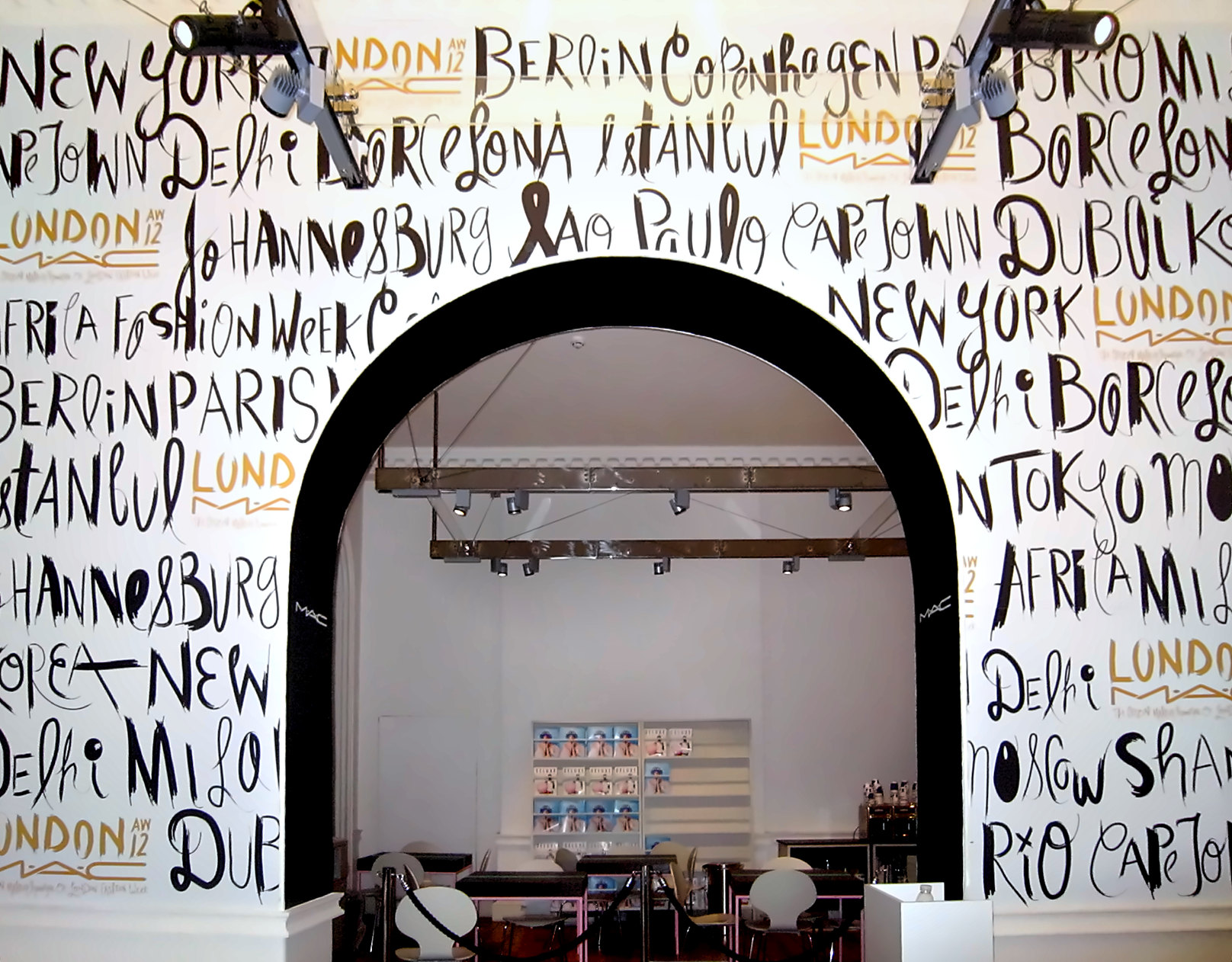 A white wall covered floor to ceiling in hand-lettered city names around an arched doorway, London Fashion Week
