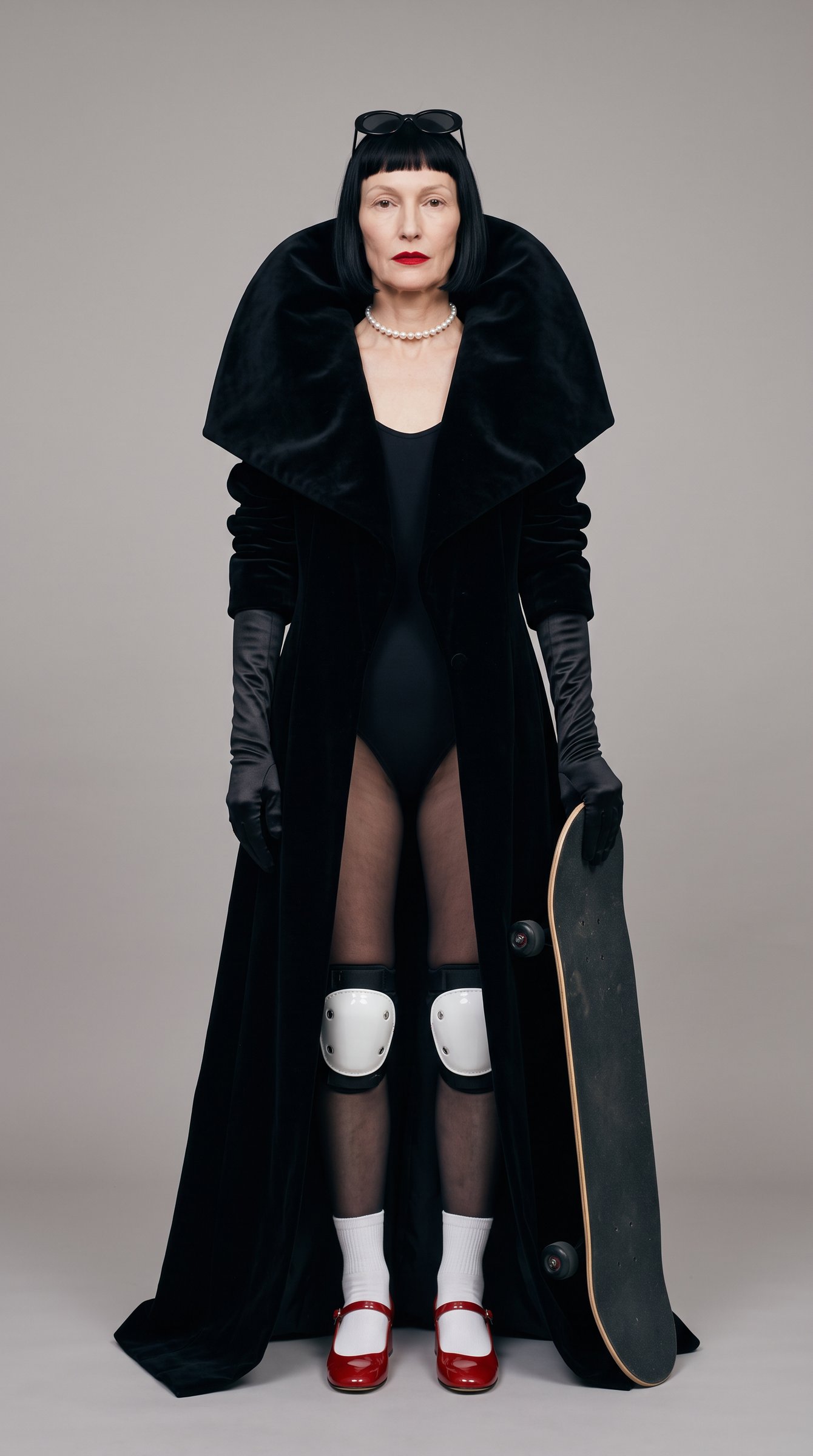 Odile in a black velvet opera coat, satin gloves and knee pads, holding a skateboard