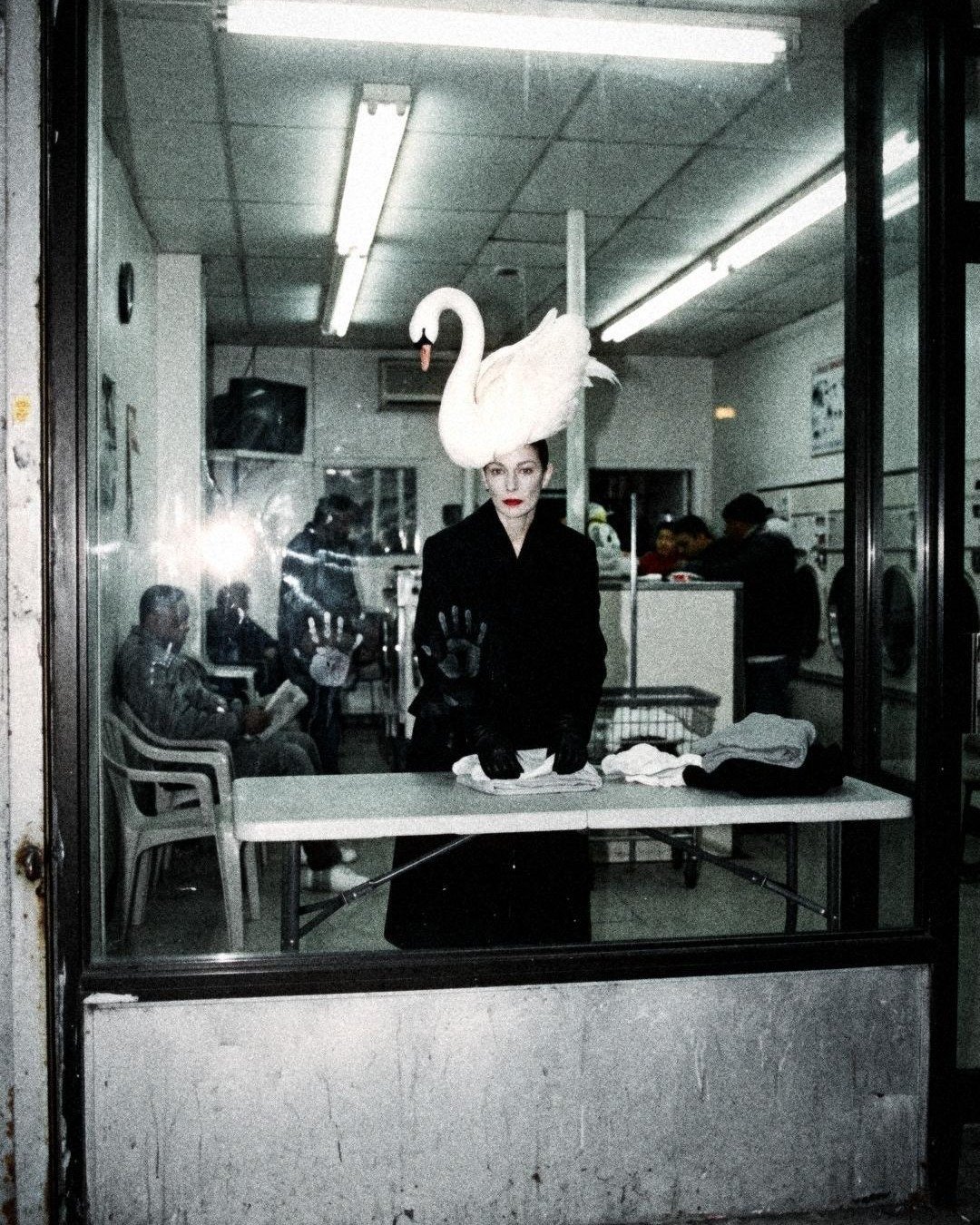 SEEN IT. Issue No. 01: Hattie, a swan on her head, folding laundry behind a laundromat window at night