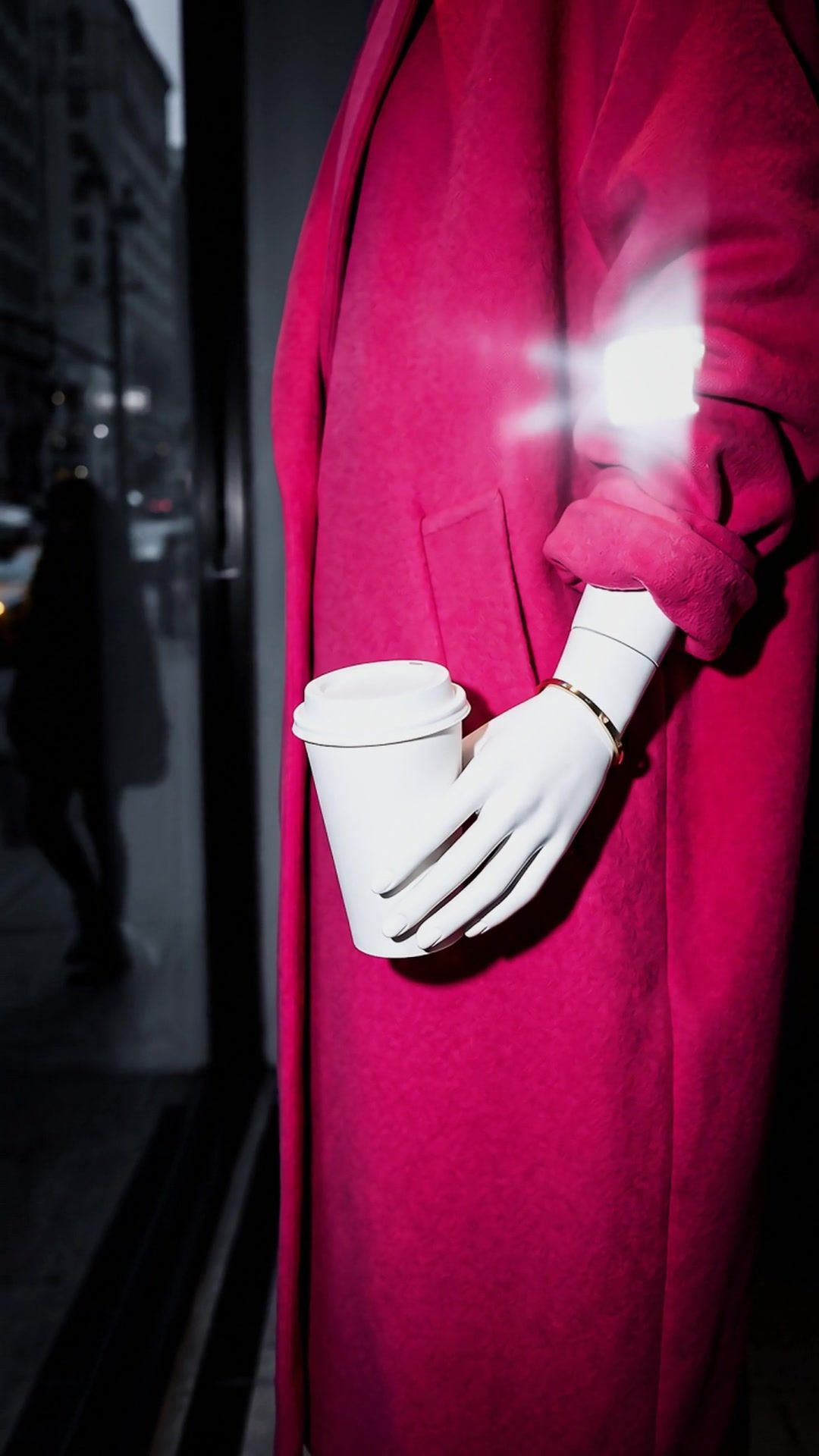Close on Fifth’s white hand holding the coffee cup against the pink coat