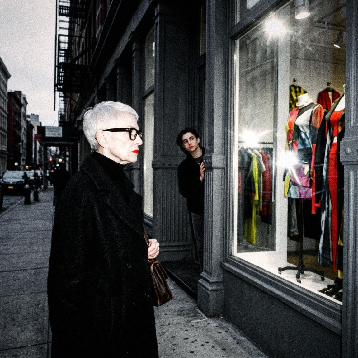 Vera, white hair and black glasses, in a black coat on the street
