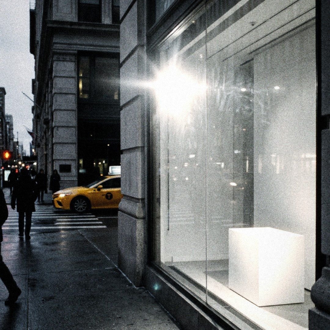 A Fifth Avenue window at dusk, flash on the glass, a yellow taxi