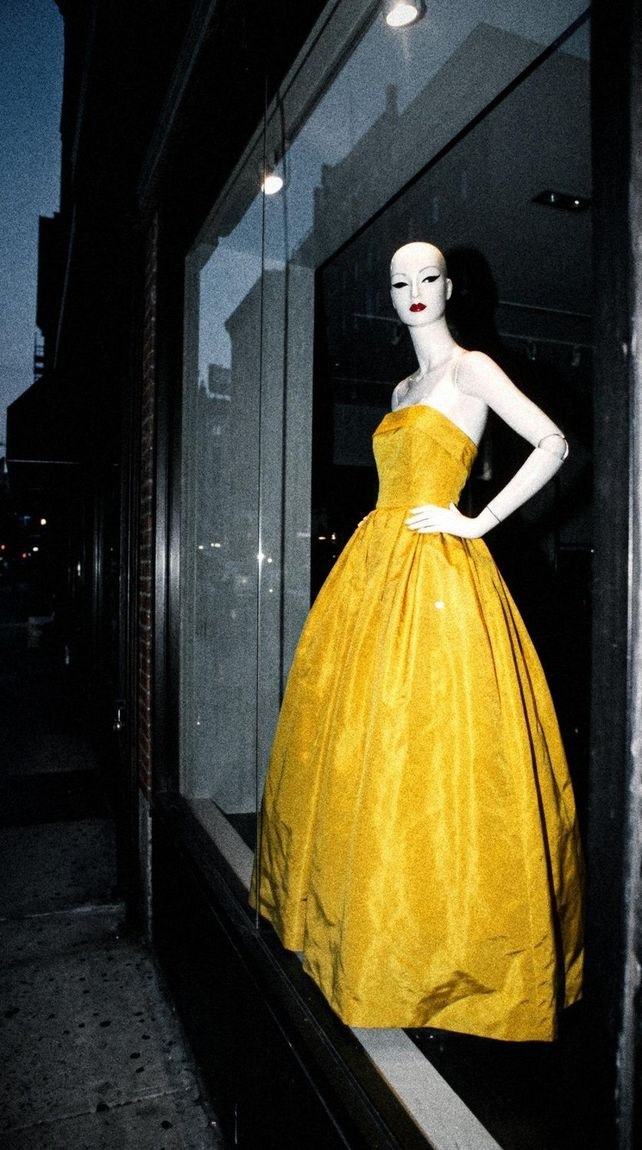 A yellow gown in a grey-blue window, the only color in the frame