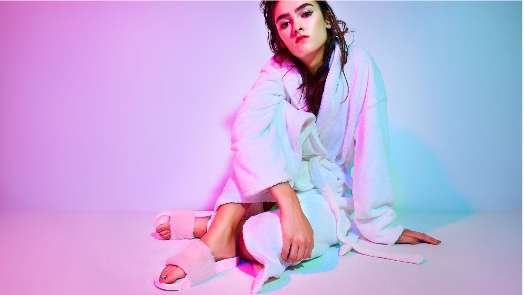 Model in a white robe and pink fur slides in pink and blue light