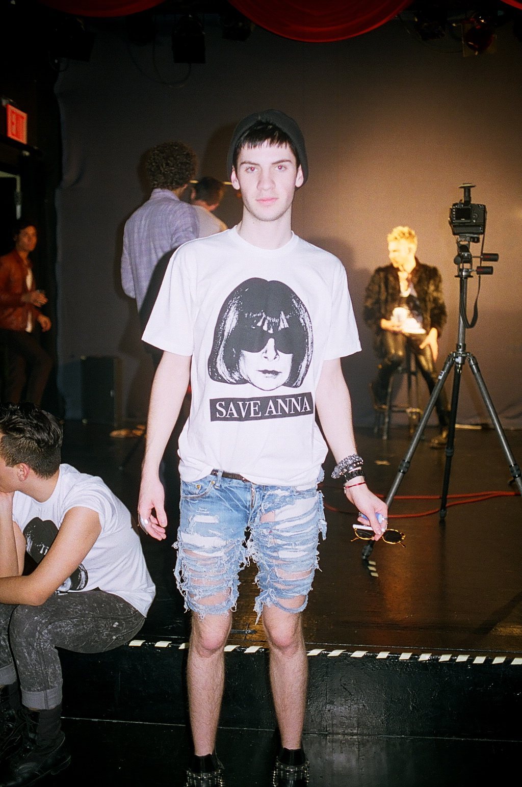 Model in a Save Anna tee and ripped denim on a club stage, shot on film
