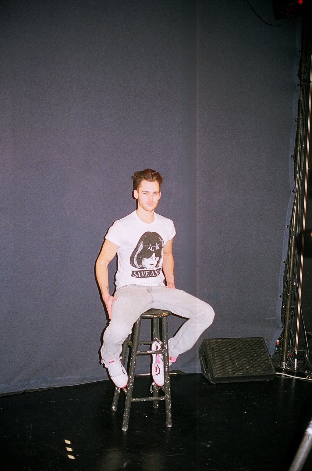 Model seated on a stool on stage in a Save Anna tee, shot on film