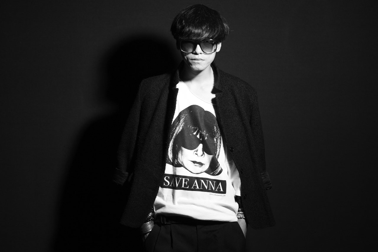 Model in sunglasses and a black jacket over the Save Anna tee, lit from one side