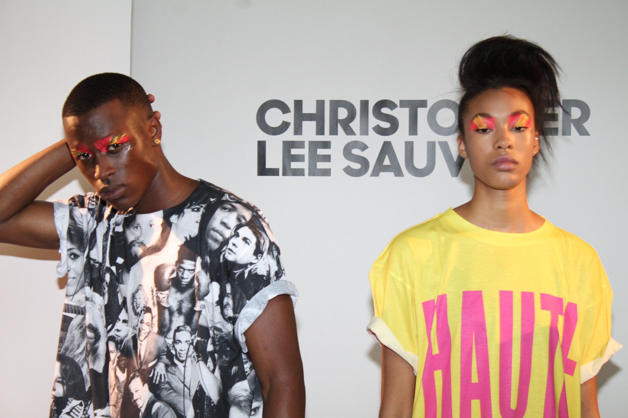 Two models with neon eye paint in a photo print tee and the HAUTE tee, in front of the Christopher Lee Sauvé backdrop