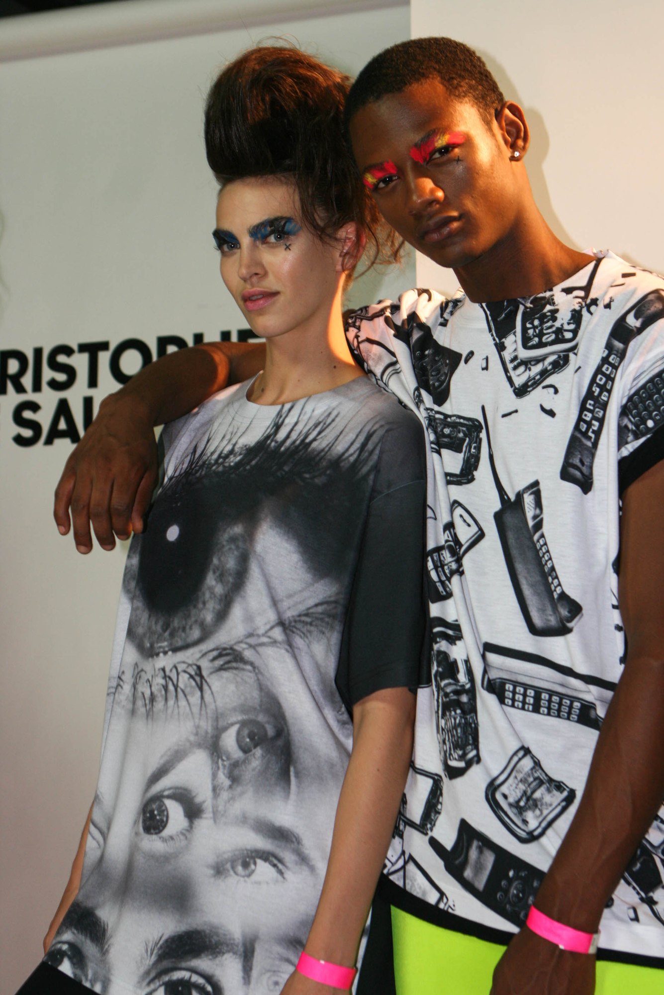 Two models leaning together in the eye print tee and a phone print tee