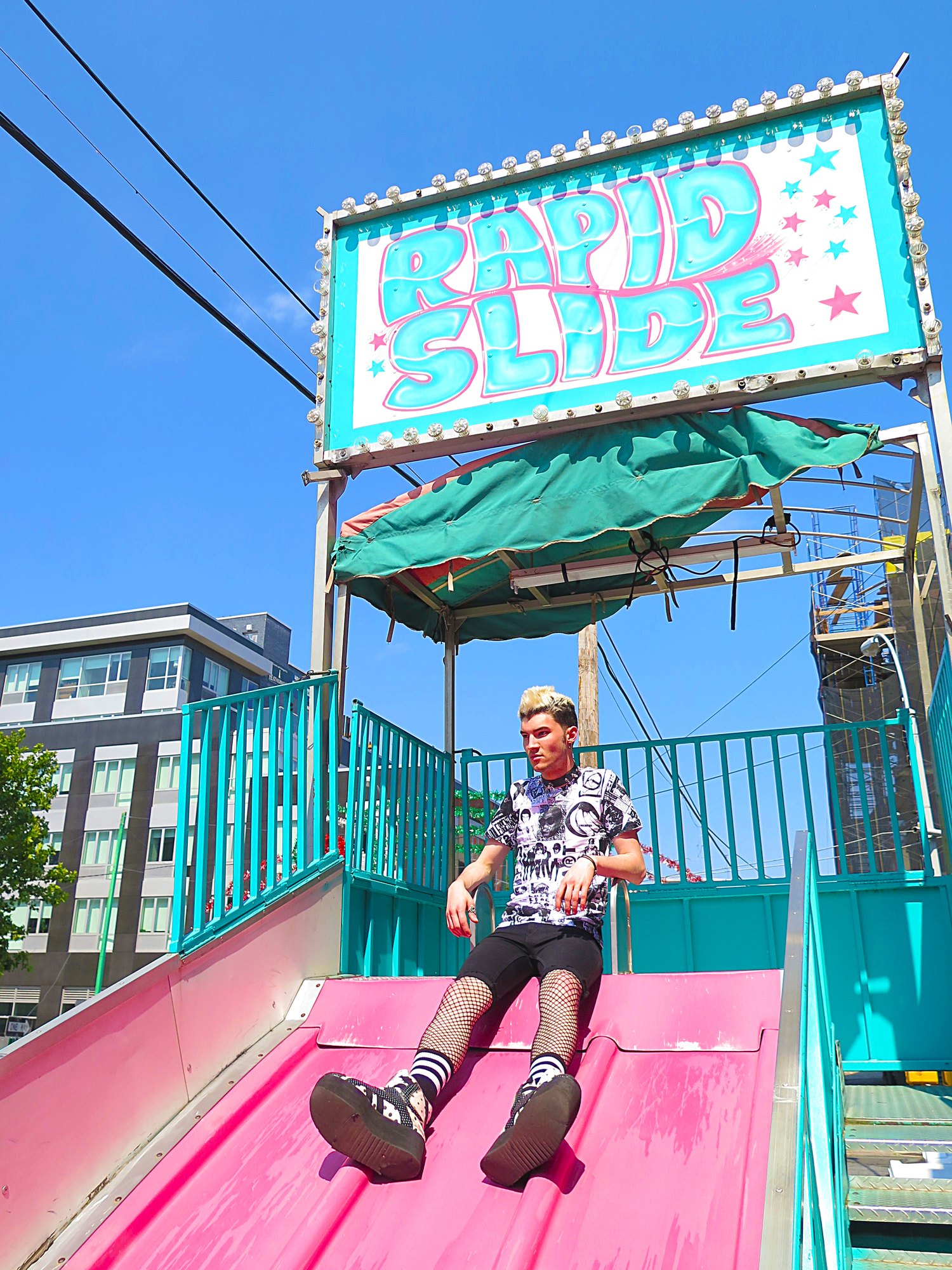 Model in a collage print tee at the top of a pink fairground slide