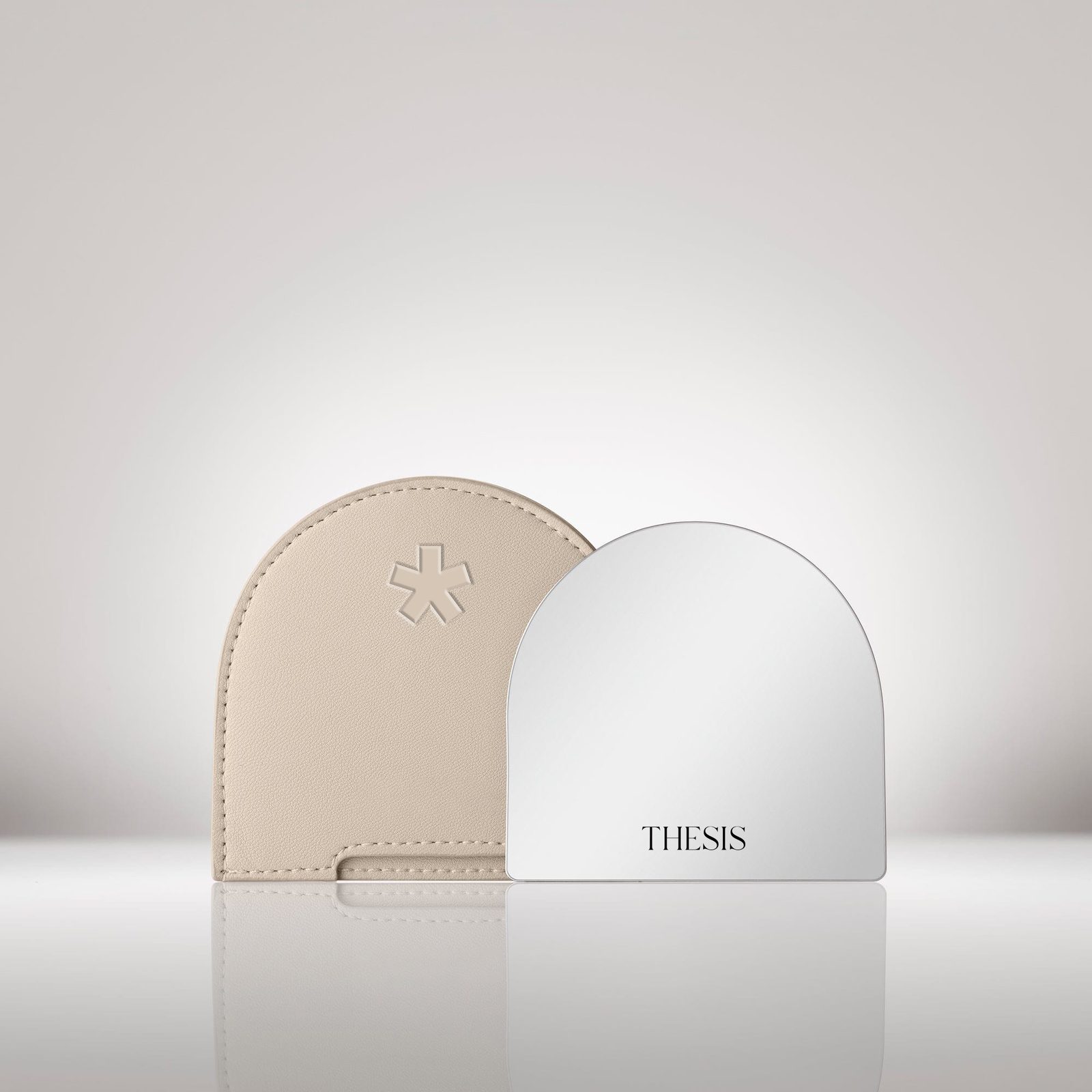 A cream leather pocket mirror debossed with the asterisk, beside a white mirror with THESIS