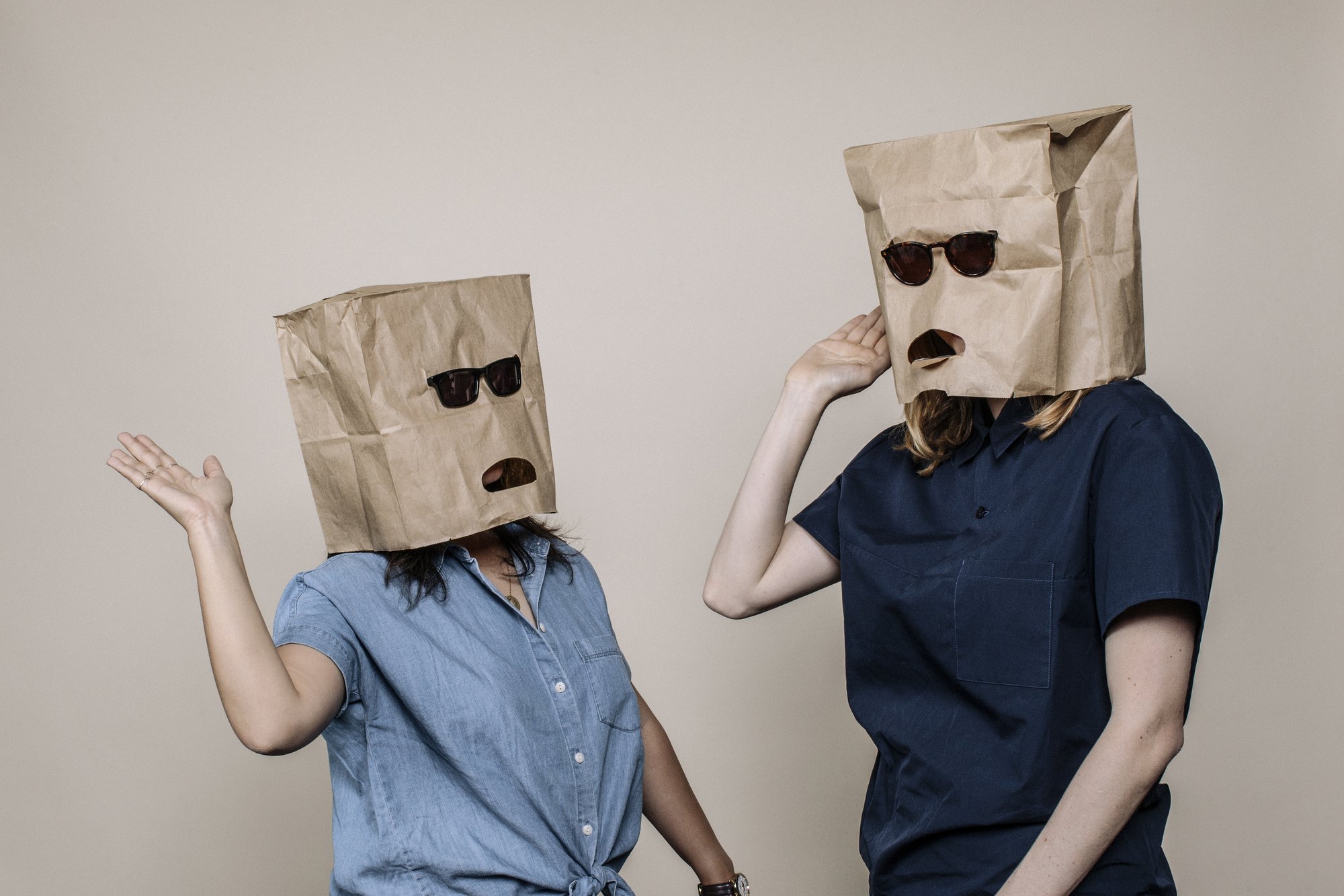 Two people with paper bags over their heads, sunglasses worn over cut-out eyes