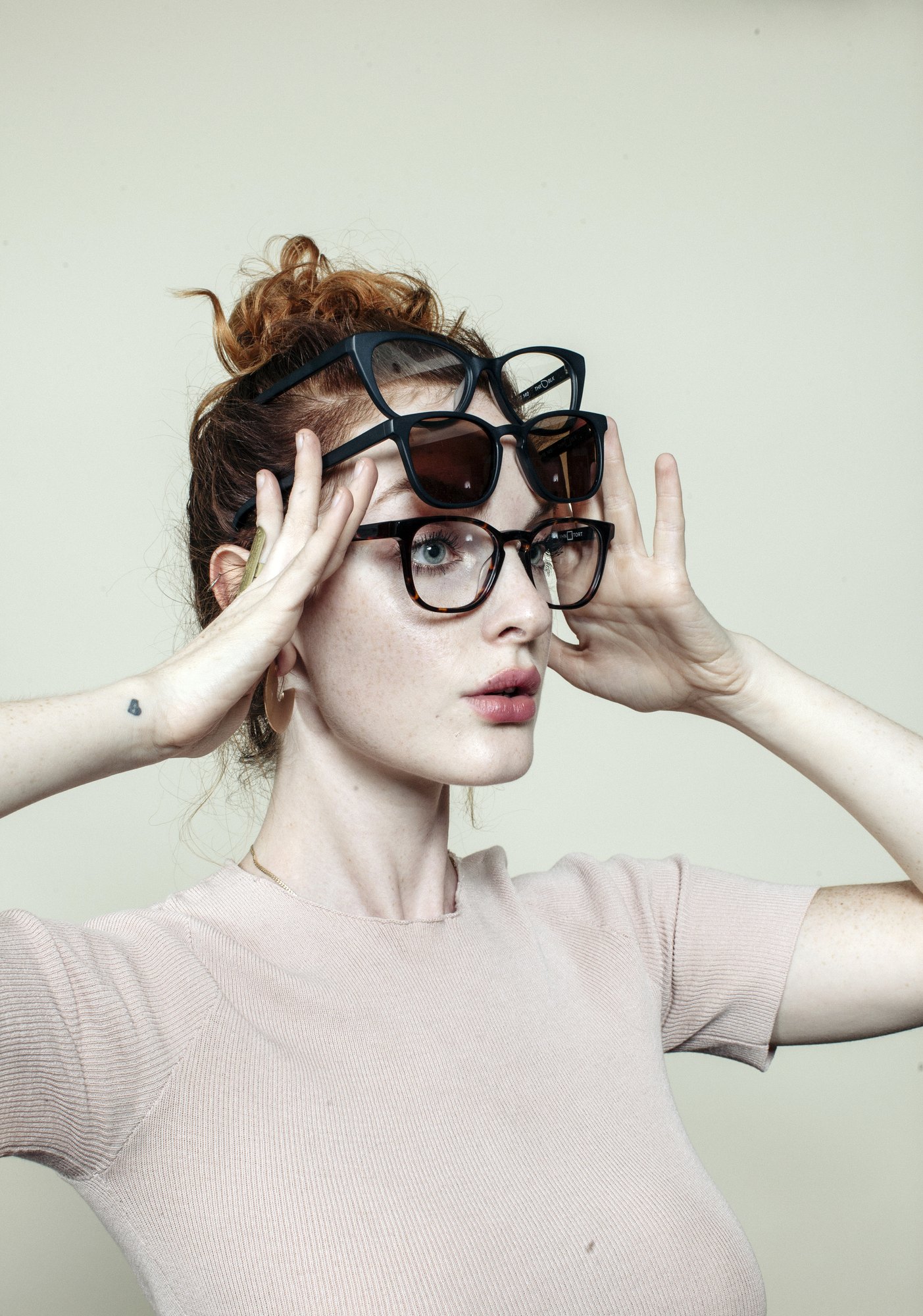 A woman with red hair wearing three pairs of Zak. frames stacked on her head
